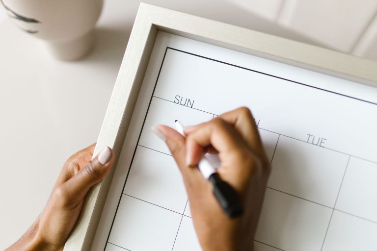Une main note un rendez-vous au feutre sur un calendrier familial encadré