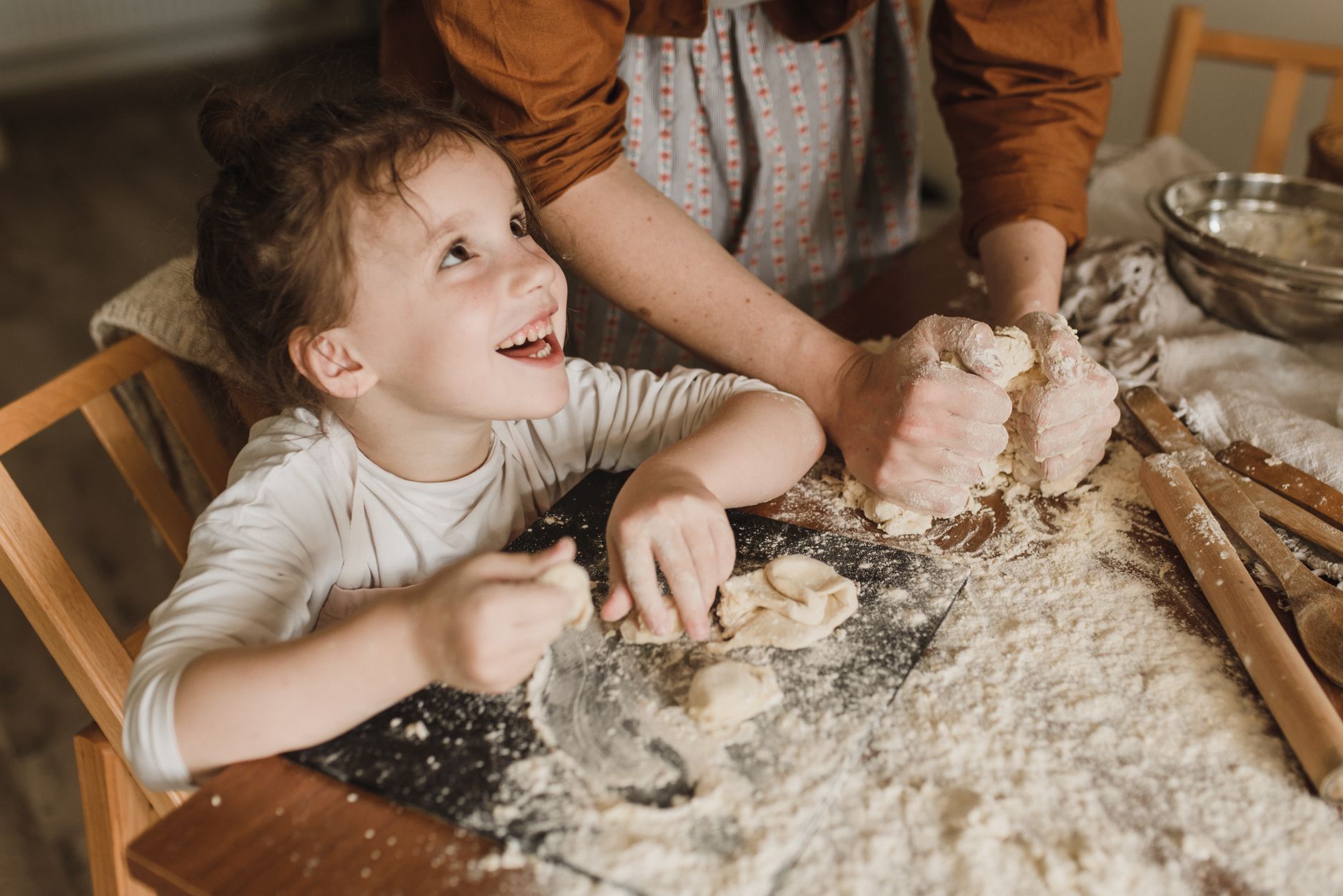 Un jeune enfant souriant pétrit de la pâte dans la farine avec un adulte, recette faite avec les enfants