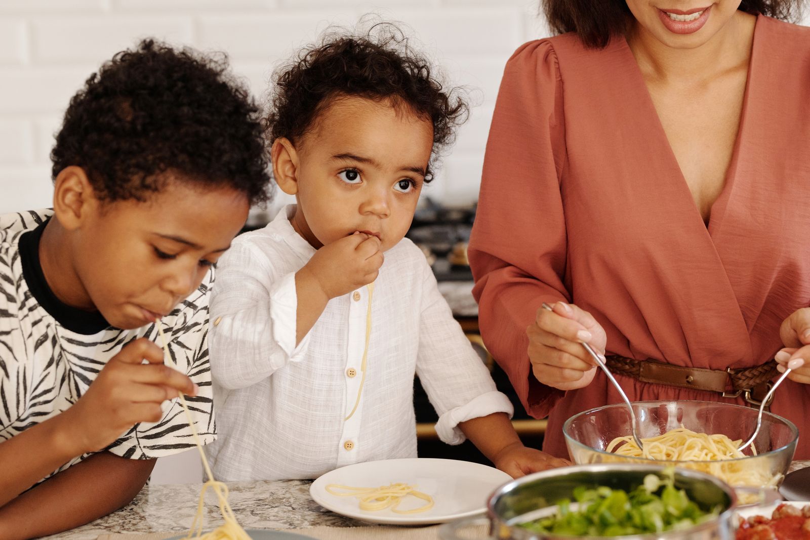 Une mère et deux jeunes enfants mangent des spaghettis et une salade à la table de la cuisine
