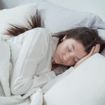 Une femme dort sur le côté, la tête posée sur un oreiller blanc dans un lit