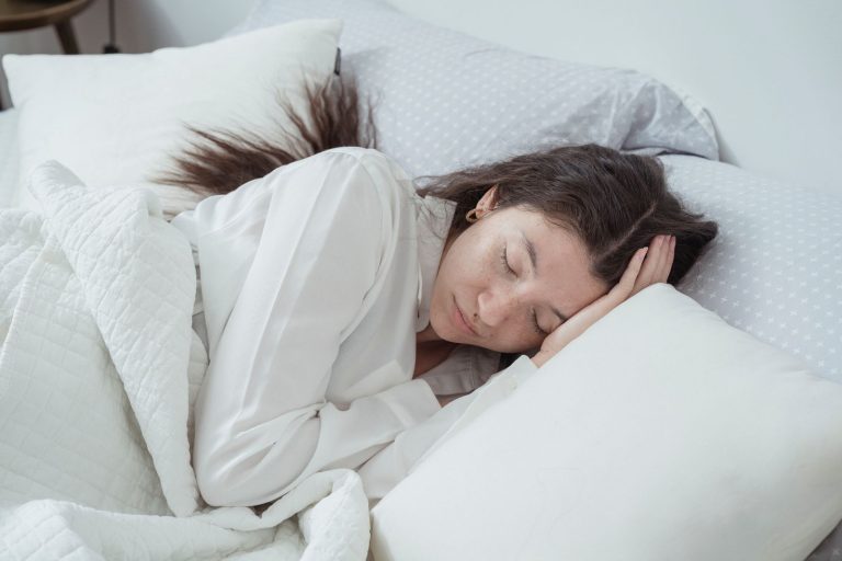 Une femme dort sur le côté, la tête posée sur un oreiller blanc dans un lit
