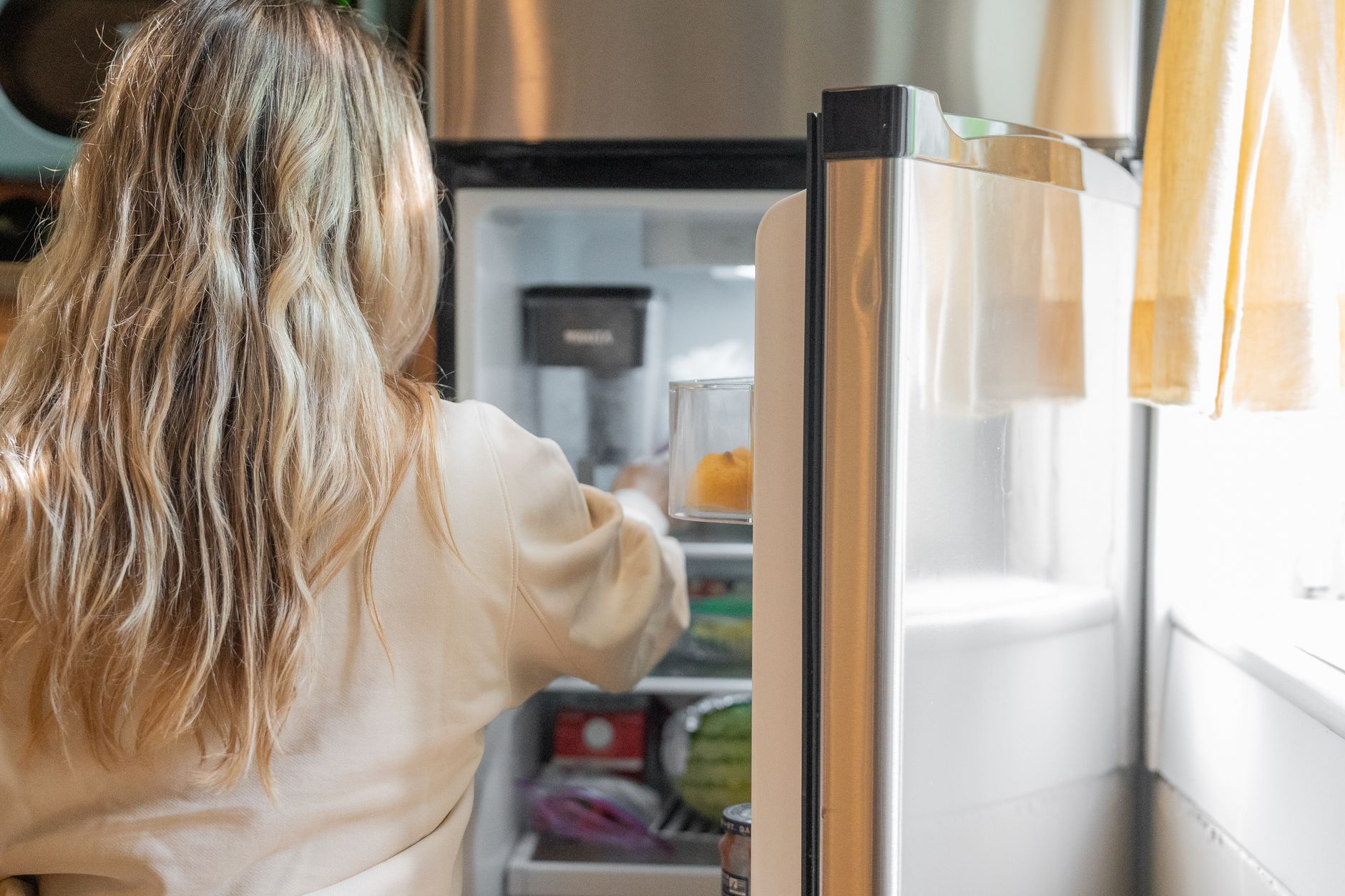 Une femme devant un réfrigérateur ouvert dont on voit les étagères