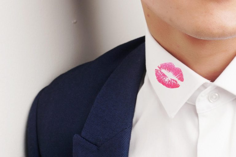 Gros plan sur un col de chemise blanche marqué d'une tache de rouge à lèvres