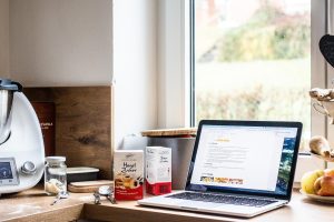 Un robot Thermomix sur un plan de travail de cuisine à côté d'un ordinateur portable affichant une recette