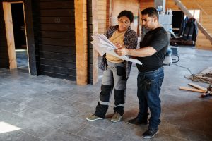 Un artisan et une cliente examinent des plans dans une maison en cours de rénovation