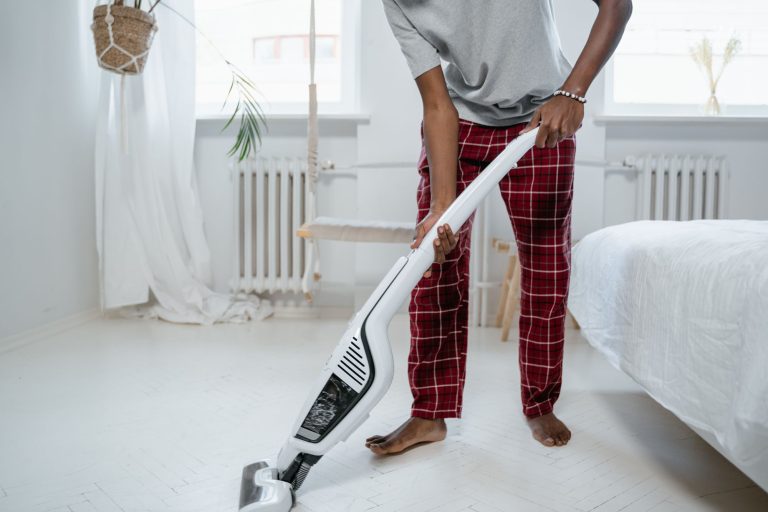 Une personne passe un aspirateur balai sans fil blanc sur le sol d'une chambre lumineuse