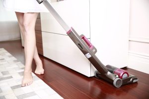 Une femme passe un aspirateur balai sans fil sur un parquet brillant