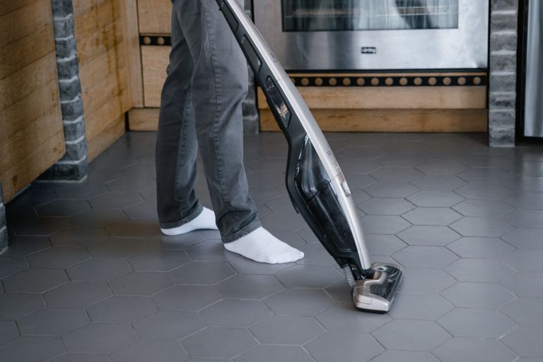 Une personne passe un aspirateur balai sans fil sur un carrelage dans une cuisine