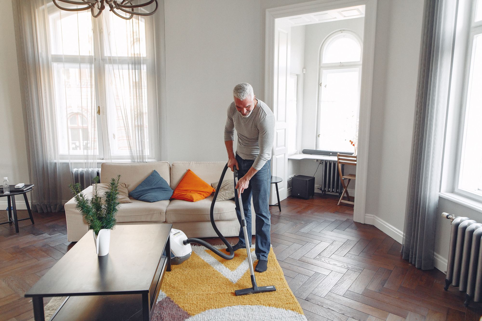 Un homme passe l'aspirateur sur un tapis dans un salon lumineux avec parquet