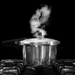Un autocuiseur en inox laissant échapper de la vapeur sur une plaque de cuisson au gaz