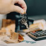 Une main tient des clés au-dessus de billets en euros et d'une calculatrice