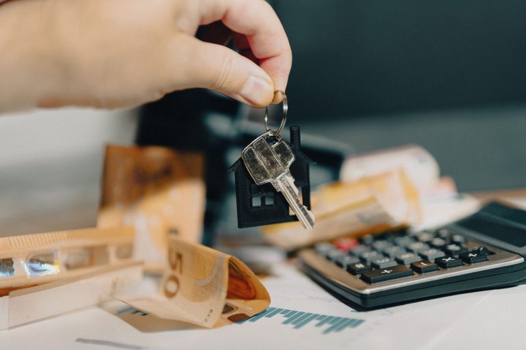 Une main tient des clés au-dessus de billets en euros et d'une calculatrice