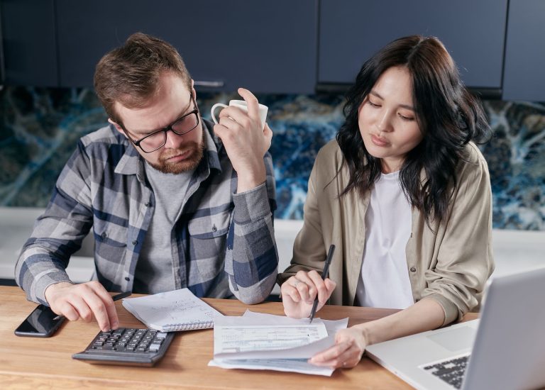Un couple fait ses comptes à la table avec une calculatrice, des factures et des papiers