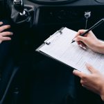 Mains remplissant un formulaire sur une planchette dans l'habitacle d'une voiture