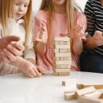 Deux enfants et des adultes construisent une tour de blocs de bois Jenga autour d'une table, un jeu sans écran