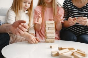 Deux enfants et des adultes construisent une tour de blocs de bois Jenga autour d'une table, un jeu sans écran