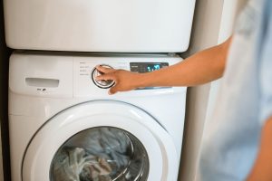 Une main tourne le bouton de programme d'un lave-linge blanc à hublot