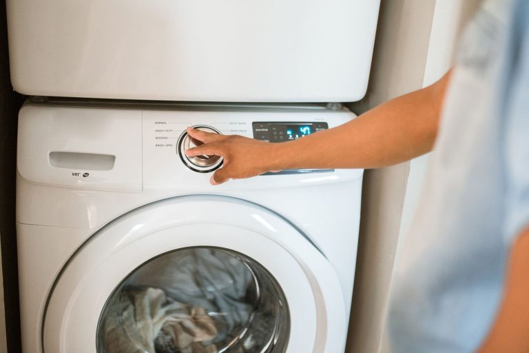 Une main tourne le bouton de programme d'un lave-linge blanc à hublot