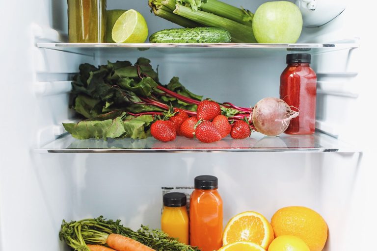 Étagères d'un réfrigérateur remplies de légumes frais, de salades, de fraises et d'agrumes