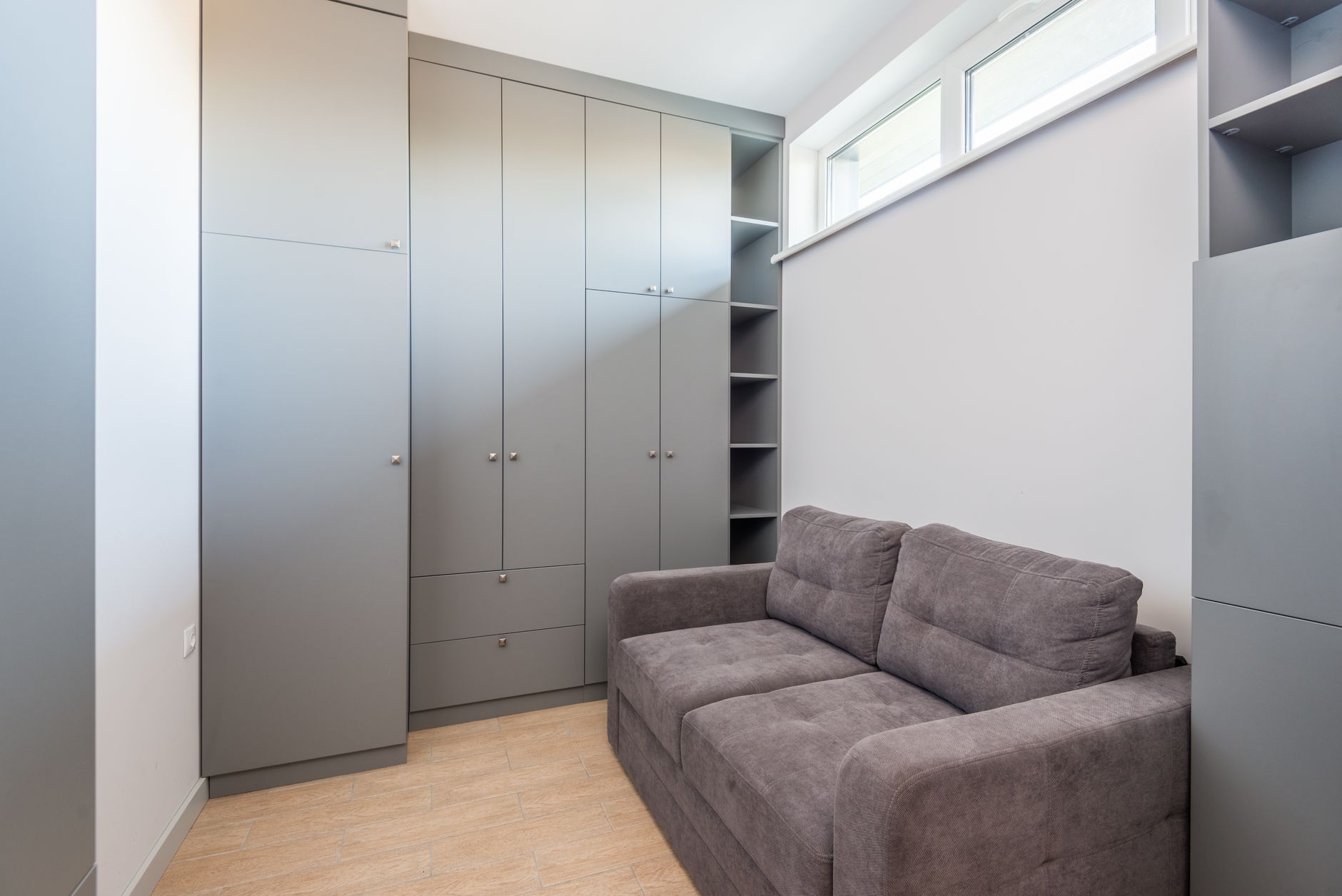 Petit salon aménagé avec un grand placard encastré gris et un canapé, exemple de rangement d'un petit appartement