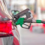 Pistolet de pompe vert inséré dans le réservoir d'une voiture aux feux arrière rouges
