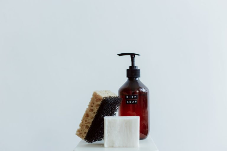 Flacon de savon noir liquide, éponge et pain de savon posés sur un fond clair