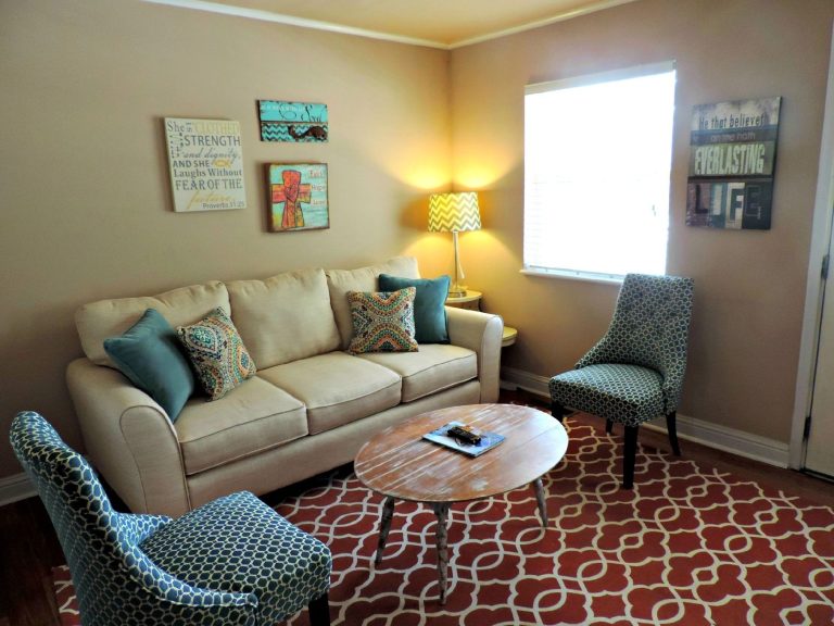 Salon avec un canapé beige et un grand tapis à motifs rouges et blancs