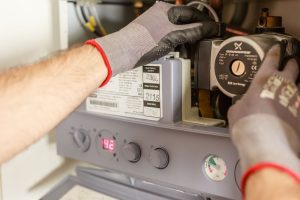 Les mains gantées d'un technicien règlent le circulateur et les commandes d'une chaudière