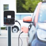 Une voiture électrique de ville branchée sur une borne de recharge murale sur un parking