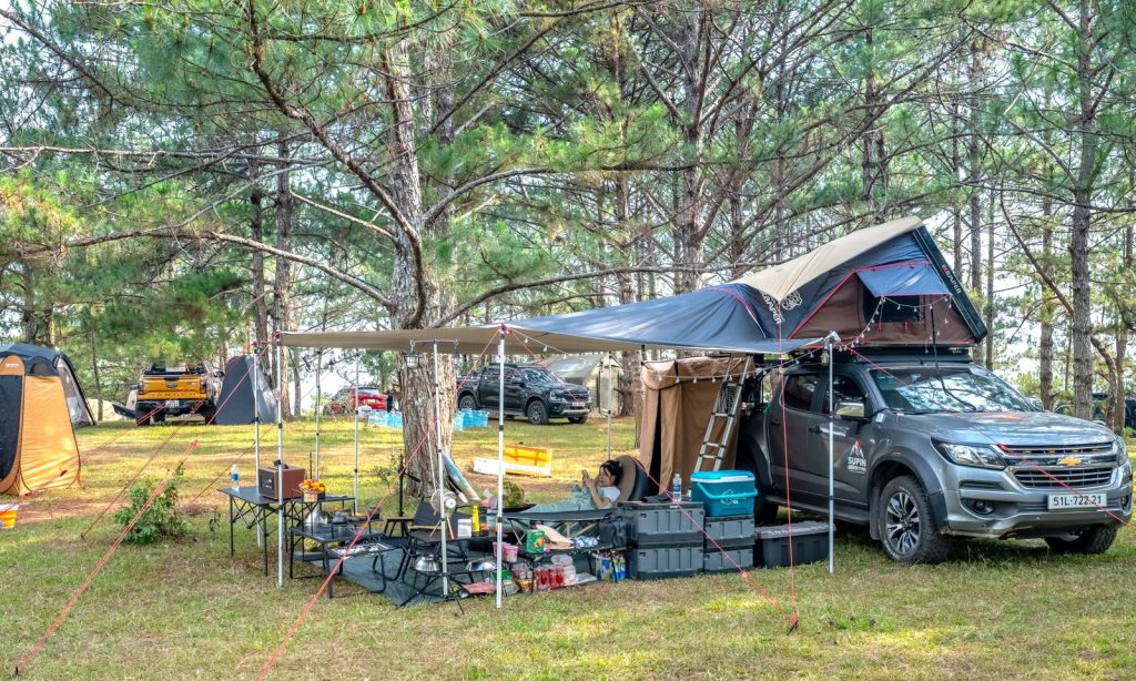 Un 4x4 équipé d'une tente de toit et d'un auvent installé sur un camping en forêt