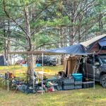 Un 4x4 équipé d'une tente de toit et d'un auvent installé sur un camping en forêt