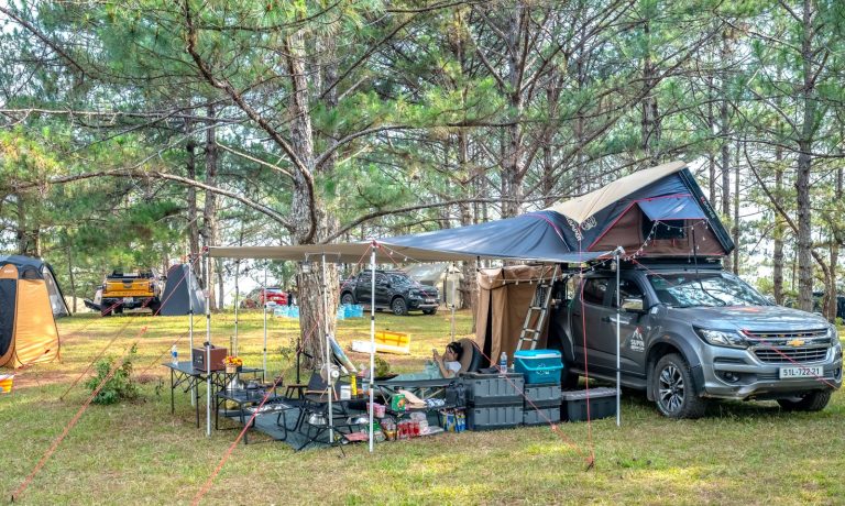 Un 4x4 équipé d'une tente de toit et d'un auvent installé sur un camping en forêt