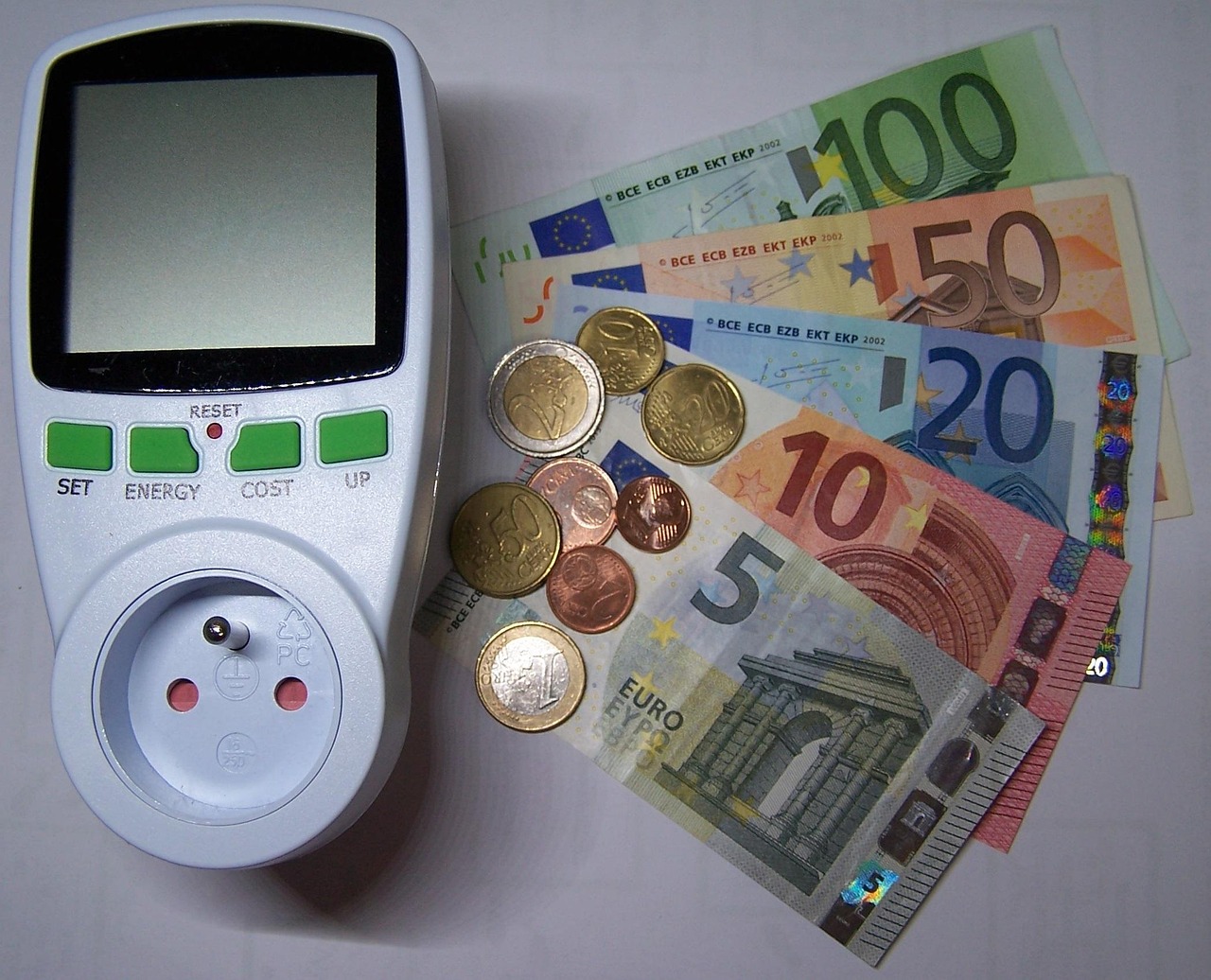 Un wattmètre branché sur une prise française posé à côté de billets et de pièces en euros