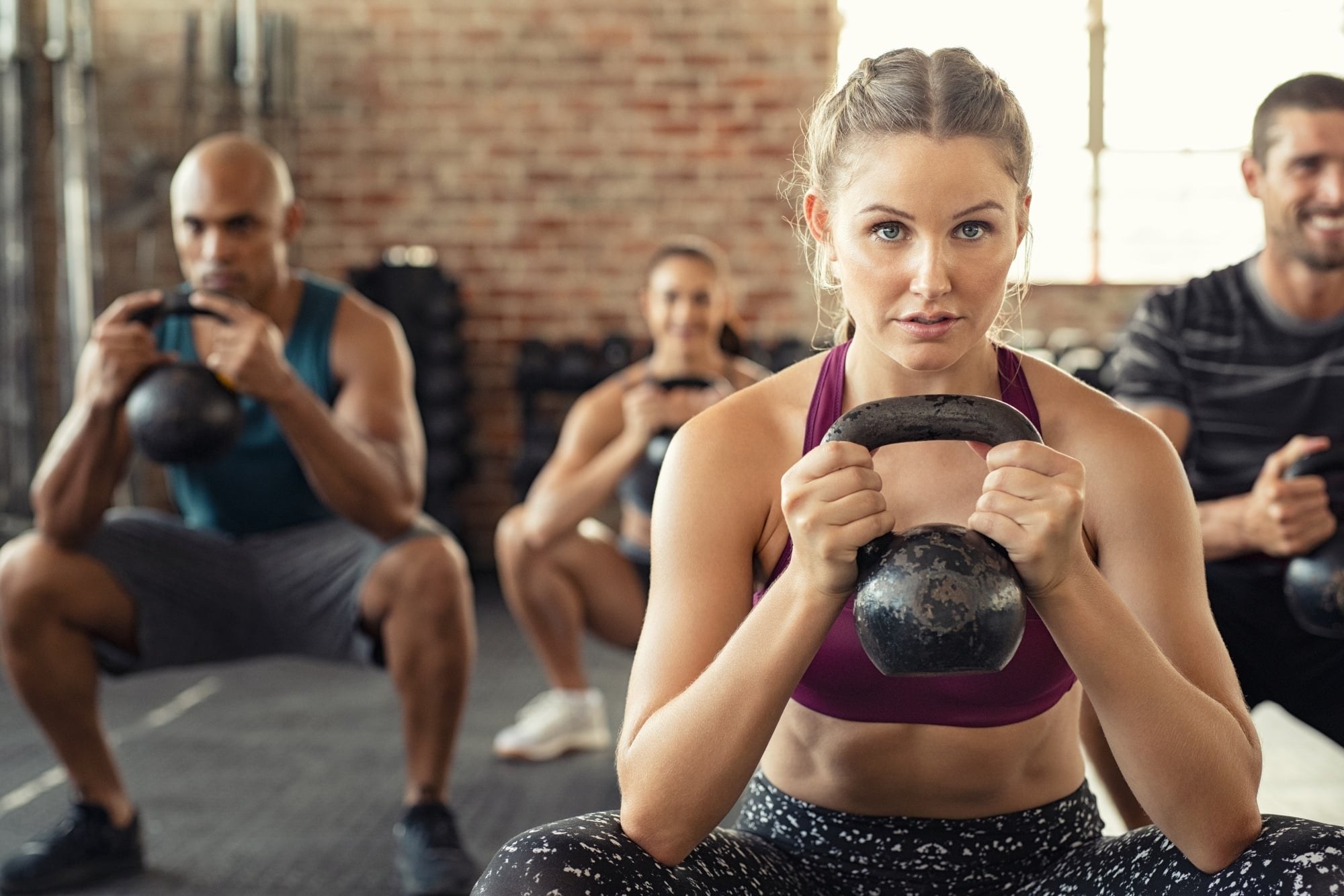Groupe mixte accroupi en salle de musculation tenant des kettlebells, femme au premier plan
