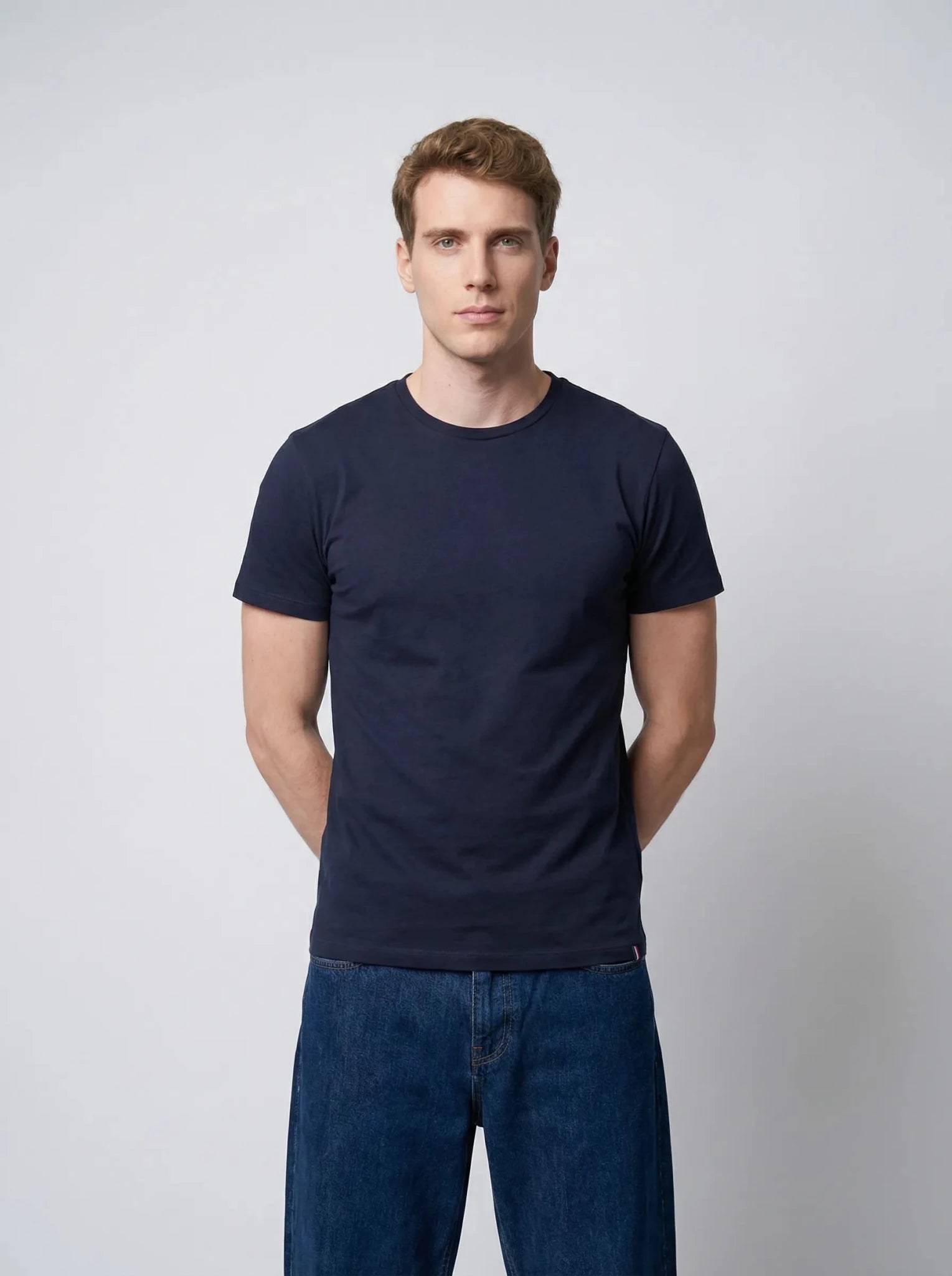 Homme portant un T-shirt bleu marine en coton, mains dans le dos, fond neutre